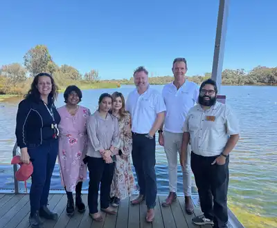 "Group gathered on wooden dock overlooking water on sunny day with clear blue sky" [G]