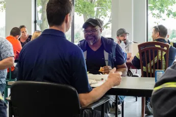 "Professionals gathered at a bright indoor meeting space, discussing industry topics at a round table." [G]