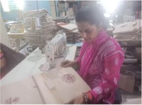 "Textile worker operating sewing machine in manufacturing workshop with stacked materials in background" [G]