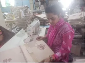 "Textile worker operating sewing machine in manufacturing workshop with stacked materials in background" [G]