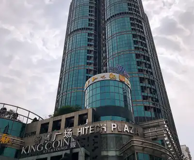 Modern glass skyscraper with King Glory Plaza and Hitech Plaza signage against cloudy sky. [G]