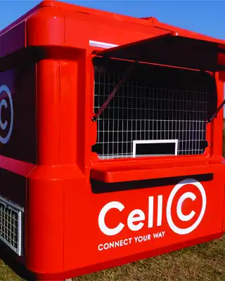 "Bright red Cell C mobile kiosk with service window against blue sky background in rural setting." [G]