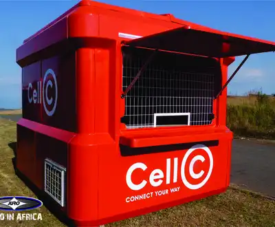 "Bright red Cell C mobile kiosk with service window against blue sky background in rural setting." [G]