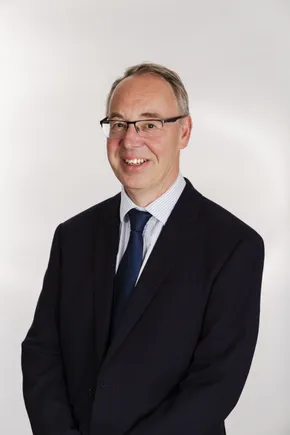 Professional portrait of a Scott Bader representative in a dark suit and blue tie against a white background. [G]