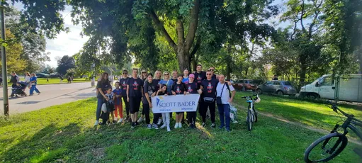 "Group gathered in a park holding Scott Bader banner during outdoor community event" [G]