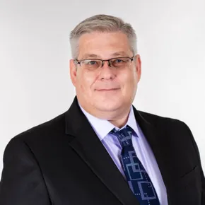 Professional portrait of a Scott Bader team member in business attire with black suit and patterned tie against white background. [G]