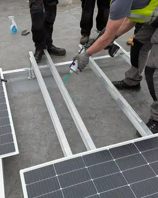 "Workers installing solar panels on metal framework using Scott Bader structural adhesives for secure mounting" [G]