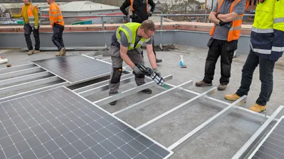 "Construction workers installing solar panels on a flat roof, using Scott Bader structural adhesives for secure mounting" [G]