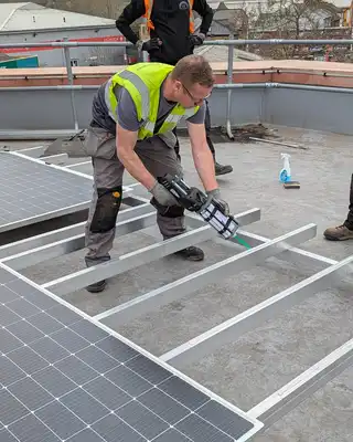 "Construction workers installing solar panels on a flat roof, using Scott Bader structural adhesives for secure mounting" [G]