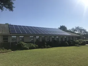 Solar panels installed on the roof of a commercial building surrounded by landscaped grounds on a sunny day. [G]