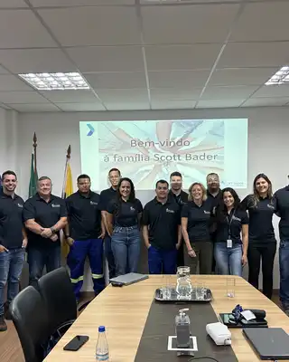 "Scott Bader team meeting in conference room with welcome presentation in Portuguese on screen" [G]