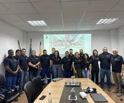 "Scott Bader team meeting in conference room with welcome presentation in Portuguese on screen" [G]