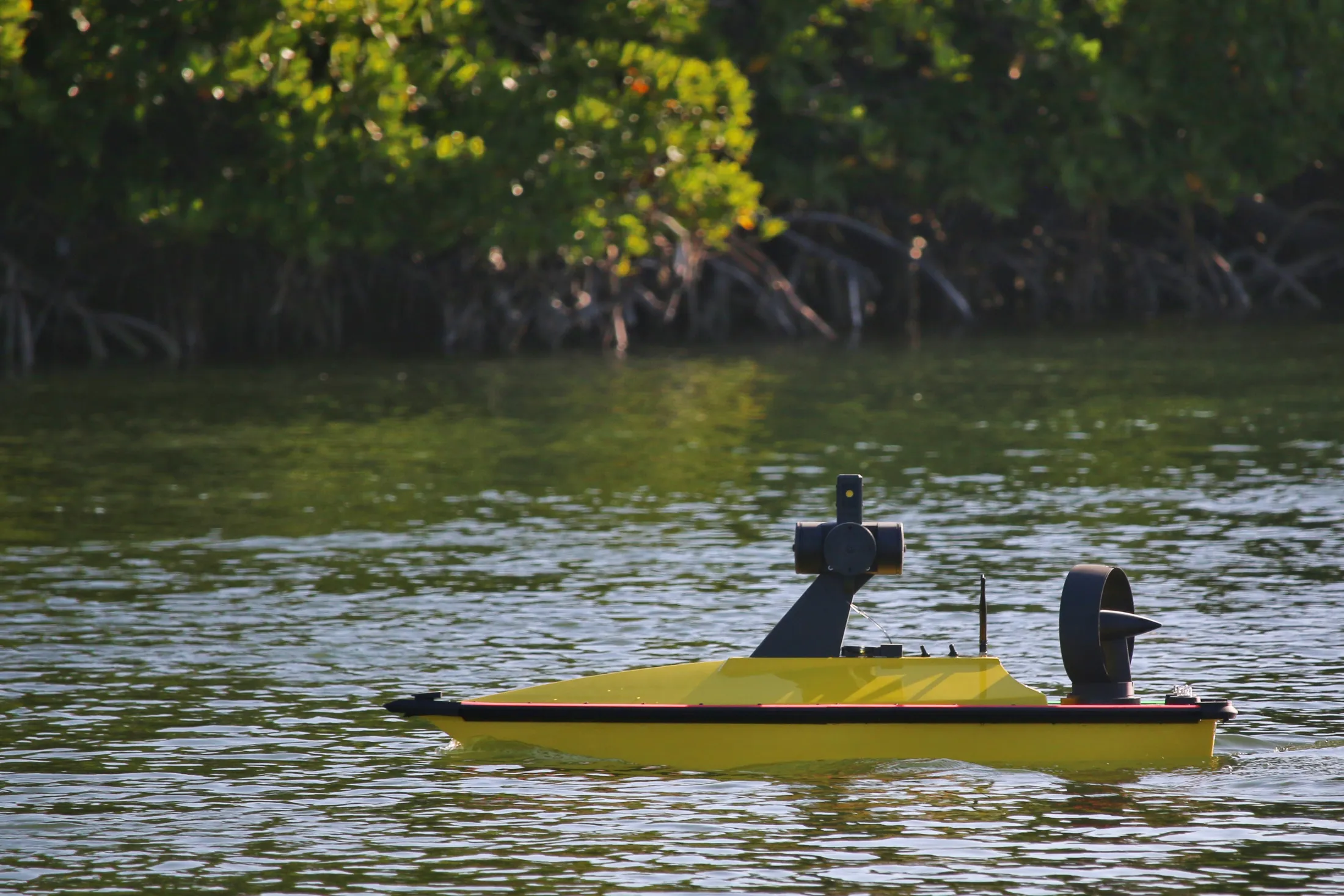 "Yellow unmanned survey boat on water with green shoreline vegetation - Scott Bader composites for marine applications" [G]
