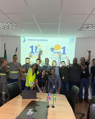 "Group celebrating 1 year milestone in conference room with Scott Bader branding on screen, team members in industrial workwear" [G]
