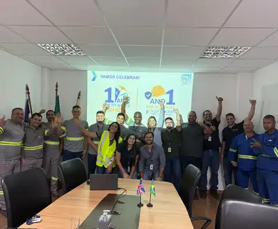 "Group celebrating 1 year milestone in conference room with Scott Bader branding on screen, team members in industrial workwear" [G]