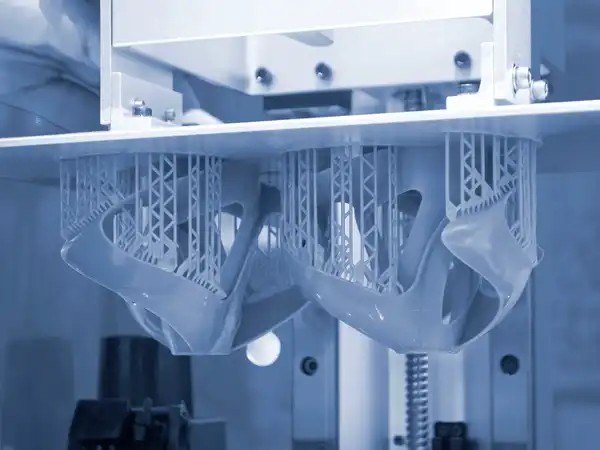 Close-up of a 3D printer creating intricate lattice structures, with two objects visible in a blue-toned image.