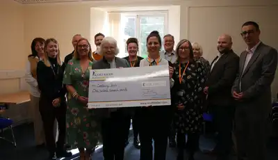 "Group presenting oversized Scott Bader check donation in bright meeting room with window view" [G]
