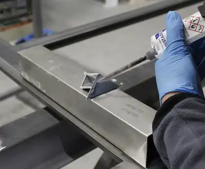 "Gloved hand applying Scott Bader structural adhesive to metal framework in manufacturing process" [G]