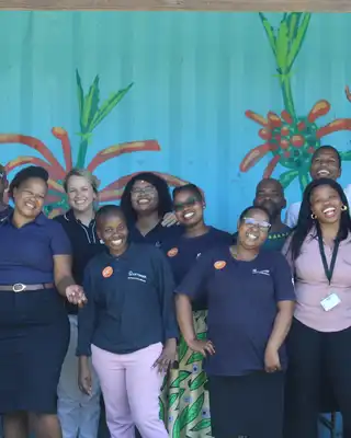 "Group of team members in navy uniforms at Scott Bader event with colorful wall mural featuring plant designs" [G]