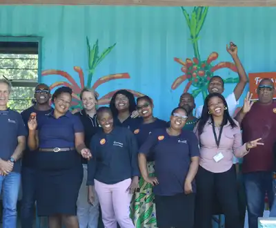 "Group of team members in navy uniforms at Scott Bader event with colorful wall mural featuring plant designs" [G]
