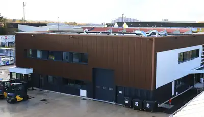 "Modern industrial facility with brown and white exterior at Scott Bader manufacturing site for composites and resins" [G]