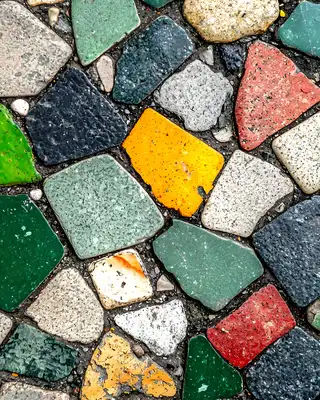 "Colorful mosaic pavement with irregularly shaped stone tiles in green, yellow, red, and black, creating a textured decorative surface." [G]