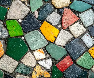 "Colorful mosaic pavement with irregularly shaped stone tiles in green, yellow, red, and black, creating a textured decorative surface." [G]