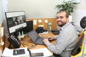 "Professional at desk with laptop and monitor displaying world map, potted plant in background in Scott Bader office environment" [G]