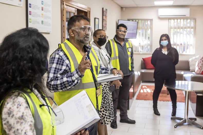 "Team in safety gear during industrial meeting at Scott Bader facility, discussing composites manufacturing processes" [G]