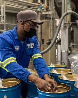 "Worker in blue uniform handling materials in Scott Bader manufacturing facility for resins and composites production" [G]