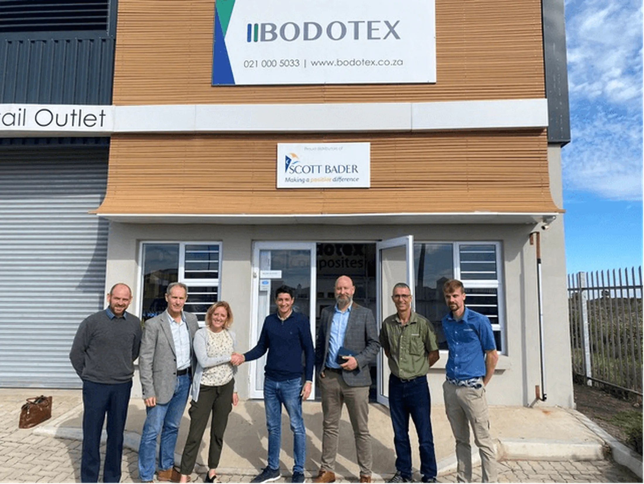 "Group of professionals standing outside Bodotex retail outlet with Scott Bader signage, specialists in composites and adhesives." [G]