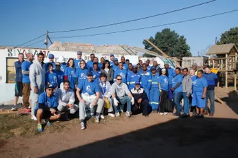 "Group in blue shirts gathered at construction site, representing Scott Bader's community outreach program" [G]