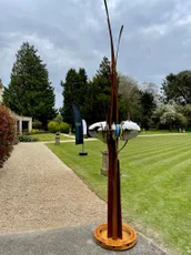"Outdoor sculpture garden with modern art installation featuring tall metal rods on a manicured lawn path" [G]