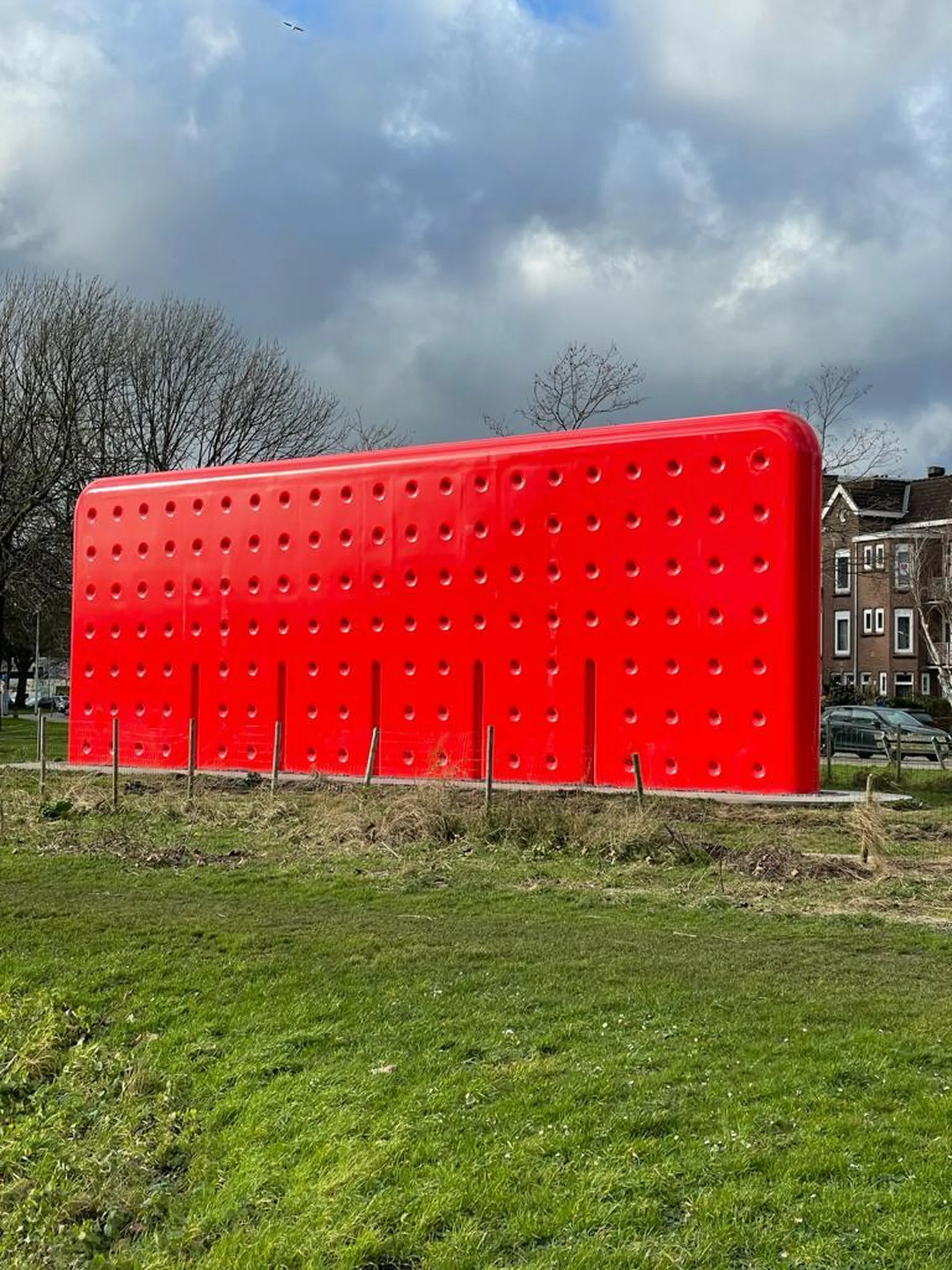 "Bright red perforated panel structure in a grassy field, showcasing durable composites by Scott Bader" [G]