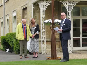 "Outdoor ceremony at historic stone building with decorative white ironwork, featuring Scott Bader representatives at formal event" [G]