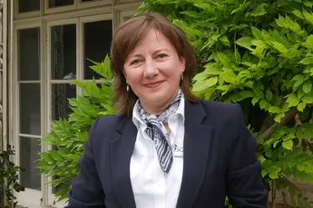 Woman in navy blazer smiling outdoors, representing Scott Bader team members. [G]