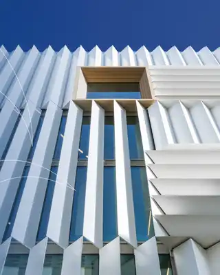 "Modern architectural building with ribbed white exterior panels against blue sky, showcasing Scott Bader composites in construction" [G]