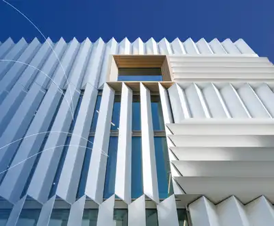 "Modern architectural building with ribbed white exterior panels against blue sky, showcasing Scott Bader composites in construction" [G]