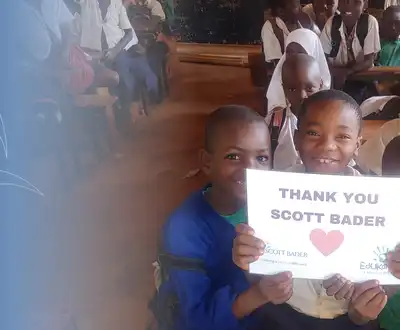 "Children in a classroom holding a 'Thank You Scott Bader' sign, showing community support for the company's initiatives." [G]