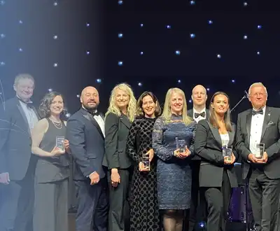 "Award ceremony with recipients holding trophies on stage against a starry backdrop, representing Scott Bader's industry recognition" [G]