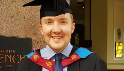 "Graduate in academic regalia with black cap and colorful hood celebrating achievement at university ceremony" [G]