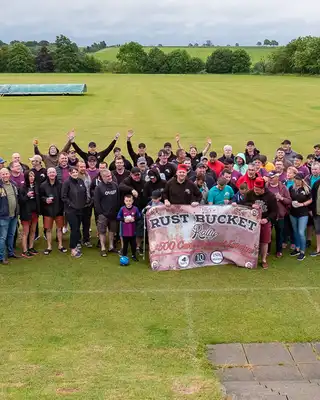 "Large group gathered on green field at Scott Bader event, displaying company banner in rural setting" [G]