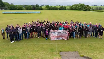 "Large group gathered on green field at Scott Bader event, displaying company banner in rural setting" [G]