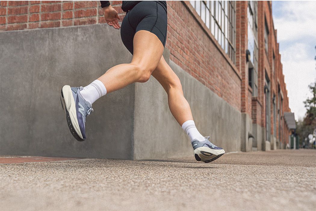 Person jogging on a city sidewalk, wearing gray running shoes and white socks, next to a brick building.