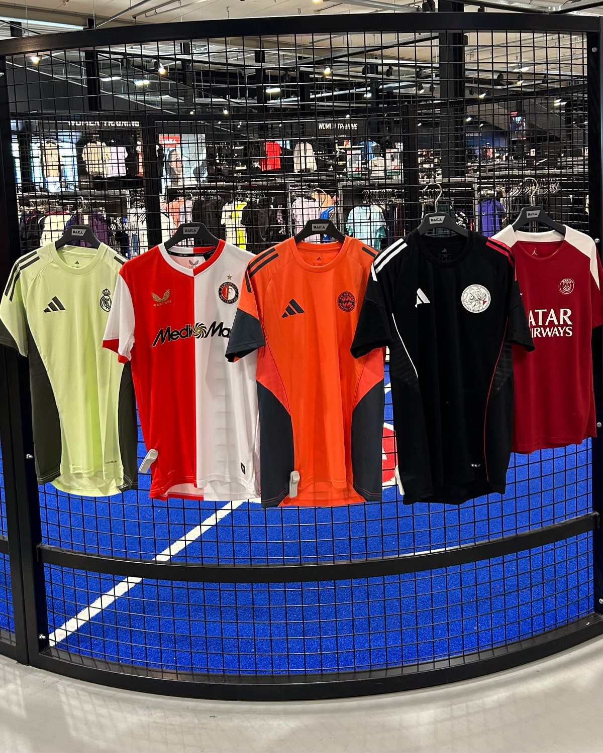 Five football jerseys hang on a wire rack in a store, with a blue sports floor visible in the background.