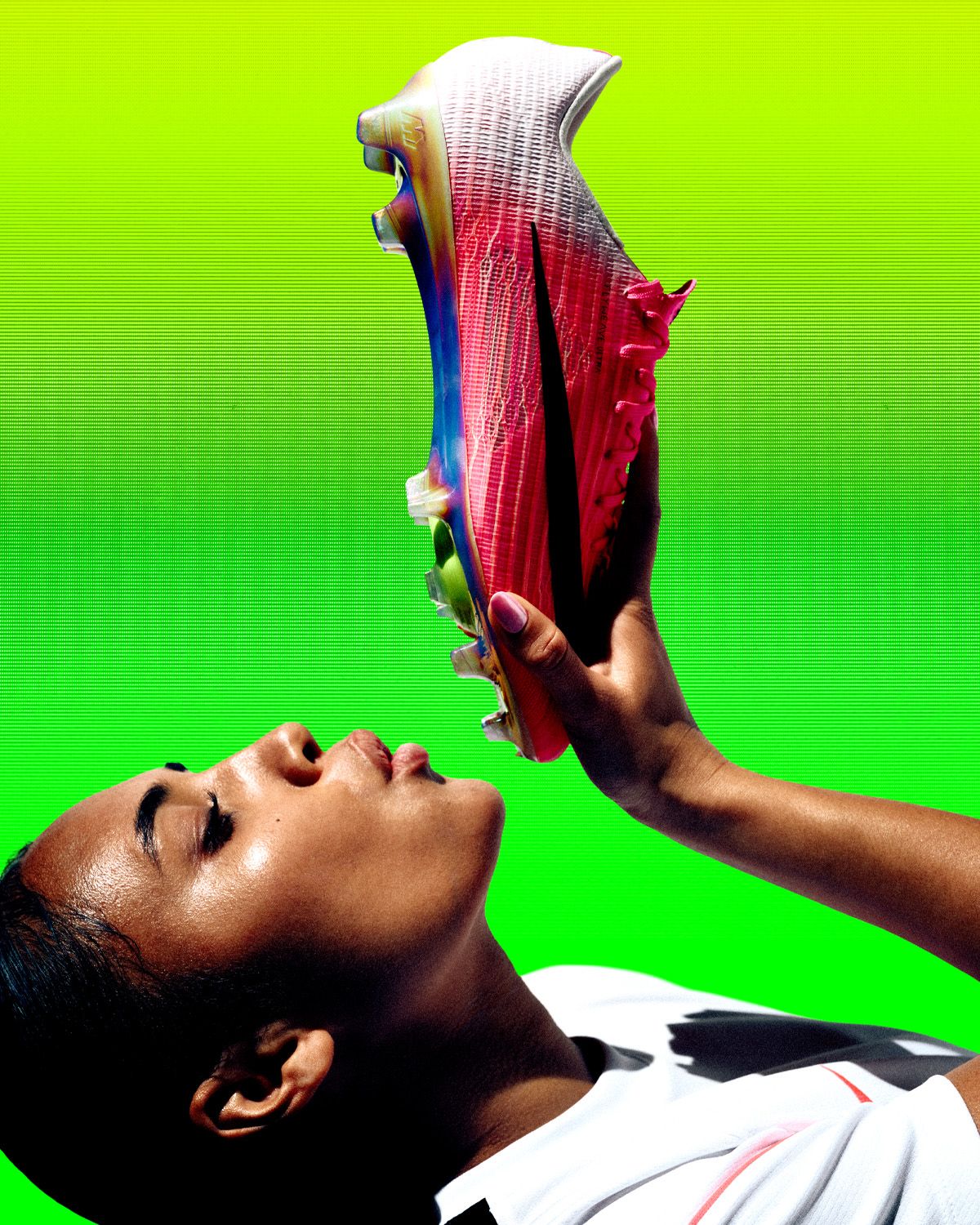 A person holding and admiring a colorful football boot against a vibrant green background.