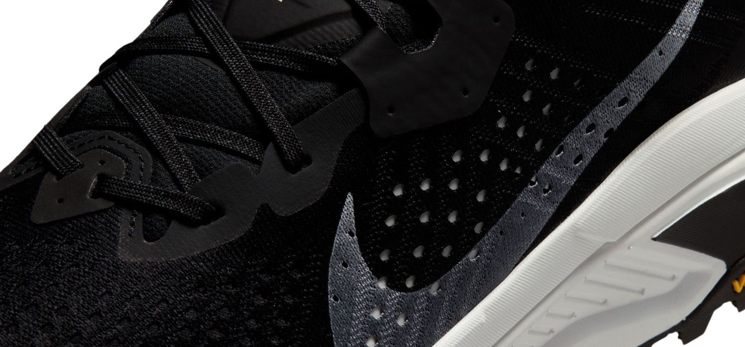 Close-up of a black athletic shoe with perforated mesh, dark laces, and a prominent swoosh design on the side.