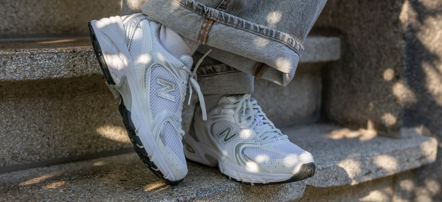Person wearing light gray sneakers and rolled-up jeans resting on outdoor stone steps in dappled sunlight.