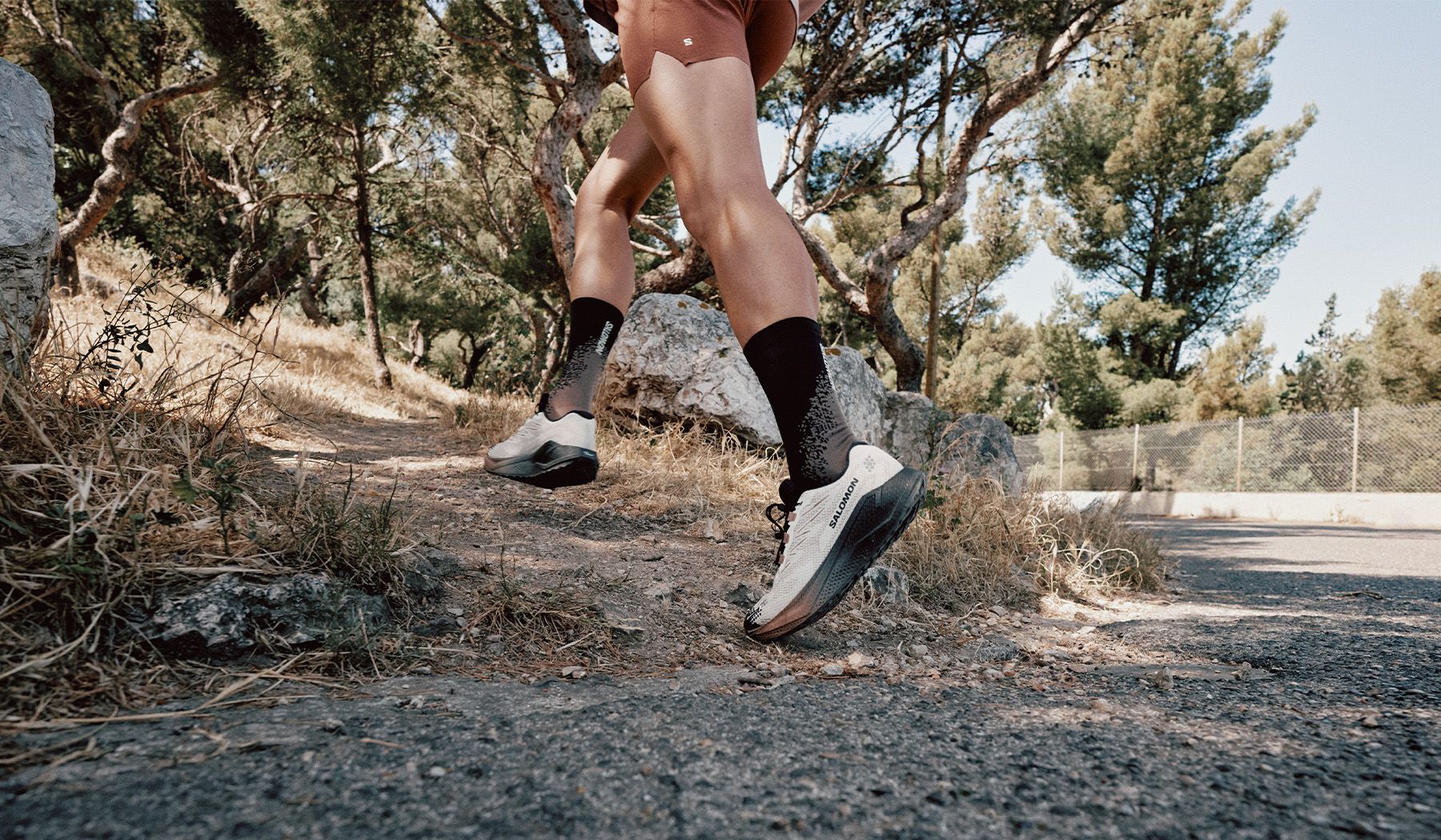 Runner with black socks and white shoes on a rocky trail in a wooded area.