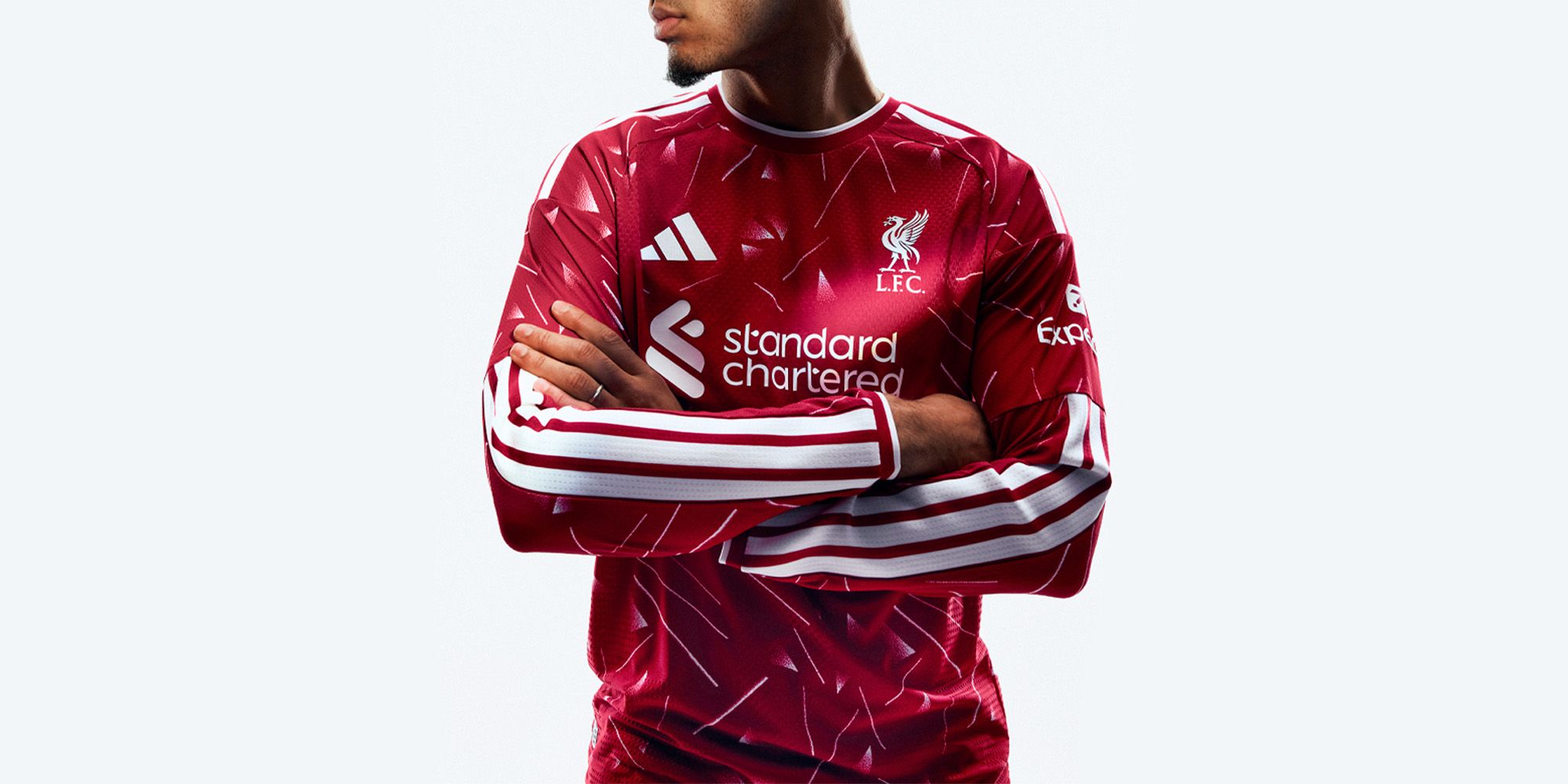Person in a red jersey with diagonal patterns, featuring L.F.C. and brand logos, arms crossed against a light background.